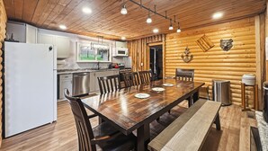 A wooden interior with a dining table, chairs, a refrigerator, a microwave, and a sink.