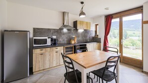 Una cocina moderna con refrigerador, microondas y estufa. Hay una mesa de comedor con sillas y un ventanal con vistas al campo.