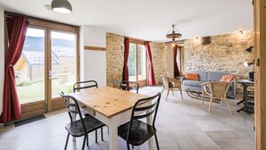 Una habitación amplia con una mesa de comedor de madera, sillas negras, un sofá gris y una pared de piedra.