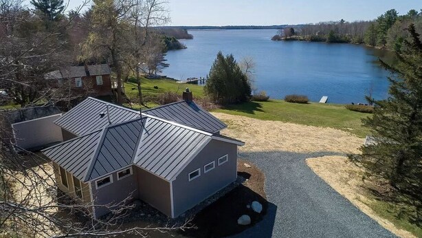 Una casa con techo inclinado y un pequeño porche, ubicada cerca de un lago con vistas despejadas.