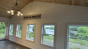 Amplia habitación con paneles de madera, lámpara de techo y varias ventanas con vistas a un lago y follaje.
