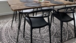 Comedor con mesa de madera, sillas negras, un jarrón con girasoles y un televisor sobre la chimenea.