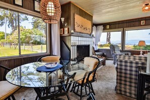 A cozy living room with a fireplace, a round glass table, and a view of the outdoors. - 6 guest  · Eddie Bauer`s former Beachfront Cottage (Sekiu)