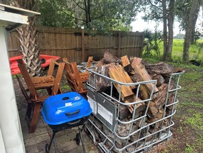 Une pile de bois de chauffage dans un porte-bois en métal, devant un bâtiment, avec une clôture en bois en arrière-plan.