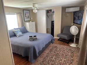 A bedroom with a bed, a chair, a standing fan, a wardrobe, and a television. - River Retreats/Anglers Paradise (Dunnellon)