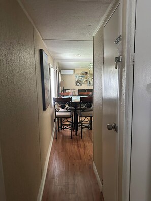 A narrow hallway with wooden flooring leading to a dining area with a table and chairs.