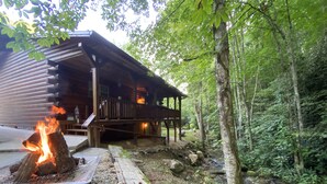 A cabin with a fire pit and a deck overlooking a forested area.