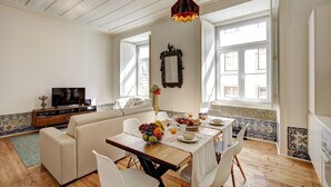 A bright living room with a wooden dining table, white chairs, a sofa, and a television. - Downtown Historic Center - Air Conditioning/Elevator (Lisboa)