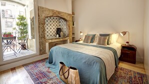 A bedroom with a bed, bedside tables, a nightstand, a patterned rug, a large window, and a view of the outside balcony. - Downtown Historic Center - Air Conditioning/Elevator (Lisboa)