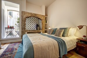 Un dormitori amb un llit, una taula de nit, una làmpada, un mur amb un disseny i vista al balcó exterior.