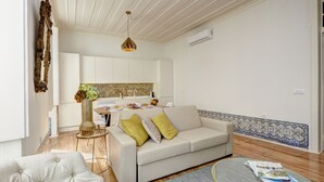 A modern living room with a white sofa, a tufted armchair, and a coffee table. A kitchen is visible in the background with white cabinets and a tiled backsplash. - Downtown Historic Center - Air Conditioning/Elevator (Lisboa)
