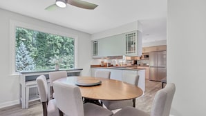 A modern kitchen with a dining area, large windows, and a view of trees.