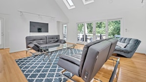 A spacious living room with a high ceiling, skylights, a gray sofa, a recliner, and a patterned rug.