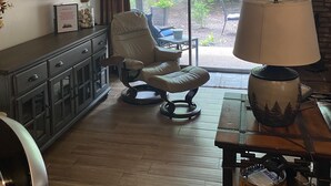 A living room with a sofa, a table with a lamp, a fireplace, a painting, and a view of greenery outside. - Beautiful condo on Pinetop Lakes Golf Course (Pinetop)