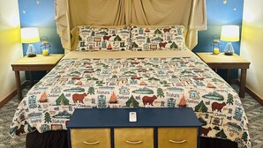 Un dormitorio con cama a dosel, pared con diseño de estrellas, ropa de cama con temática de camping, mesitas de noche con lámparas y un aparador.