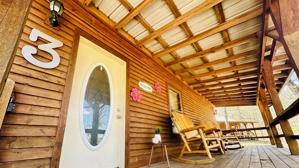 Una cabaña de madera con un porche, un letrero de bienvenida y el número 3.