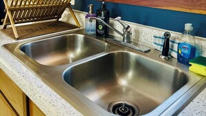 Una cocina con dos fregaderos de acero inoxidable, armarios de madera, un ventanal con cortinas y un escurreplatos.