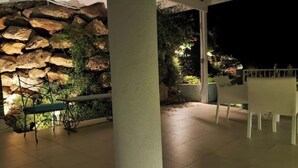 En udendørs terrasse med stenvæg, bænk og bord med stole.