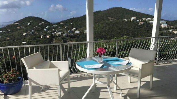 En balkon med to hvide stole og et rundt bord, med udsigt over en bakke med bygninger.