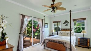 Ein Schlafzimmer mit Himmelbett, Deckenventilator und Blick auf einen Garten durch eine Schiebetür.