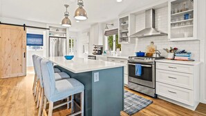 A modern kitchen with white cabinetry, a central island, stainless steel appliances, and pendant lighting. - Bluebird Hideaway (Queensbury)