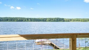 A view from a wooden deck overlooking a calm lake with a dock and a boat. - PJinx and Grace Peaceful Lake front 3BR/2ba (Shelby)