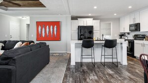 A modern kitchen with white cabinets, a black refrigerator, and a microwave. There is a dining area with two black bar stools. - PJinx and Grace Peaceful Lake front 3BR/2ba (Shelby)