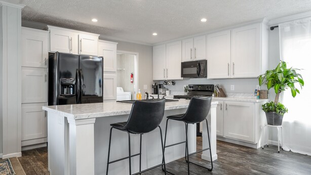 A modern kitchen with white cabinets, a black refrigerator, a microwave, and two black bar stools. - PJinx and Grace Peaceful Lake front 3BR/2ba (Shelby)
