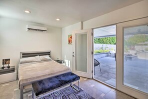 Un dormitorio con cama, mesita de noche, banco y una puerta corrediza de vidrio que da a un patio exterior.
