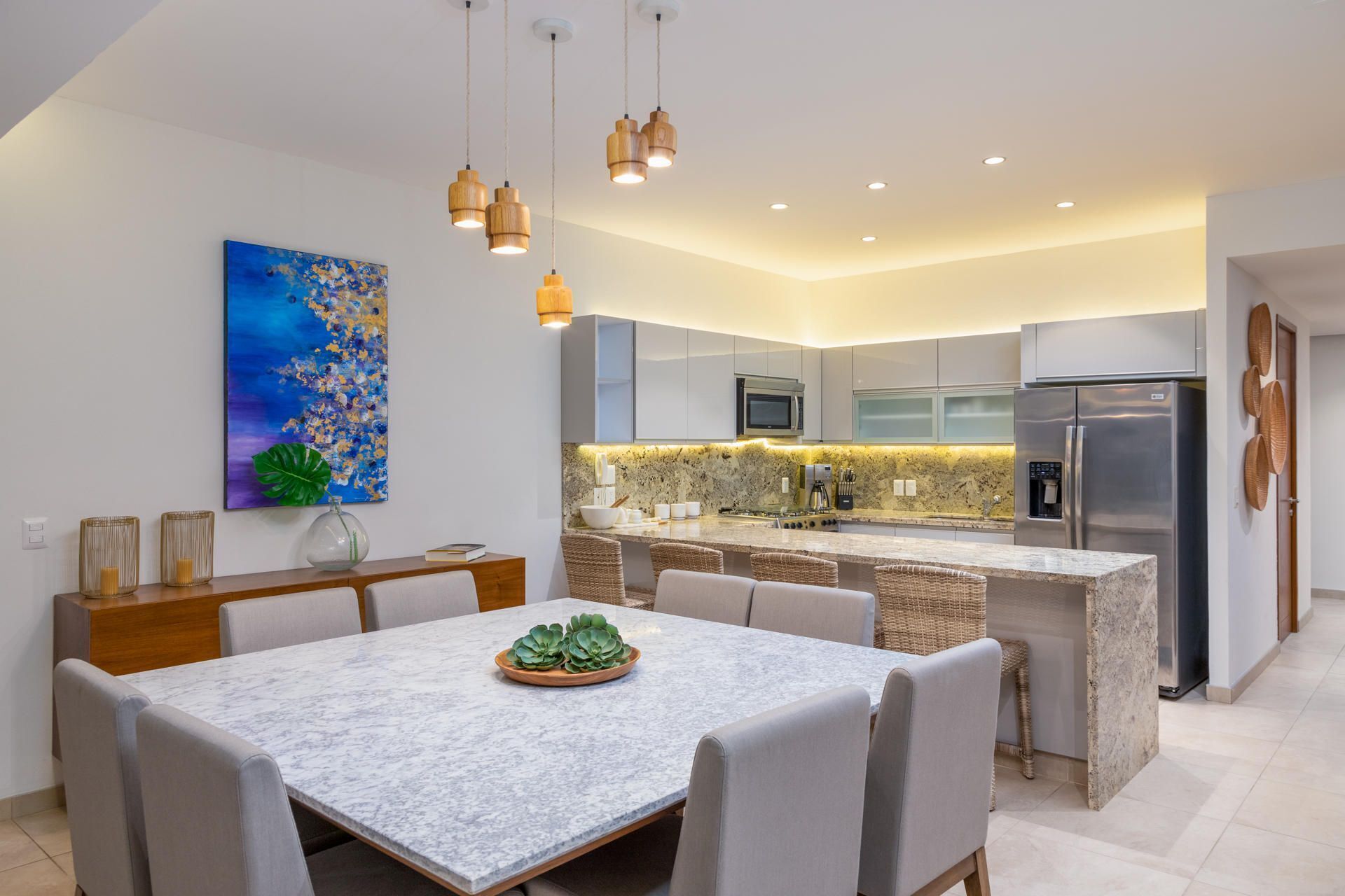 A modern kitchen with a central island, stainless steel appliances, and a dining area with a marble table and chairs.