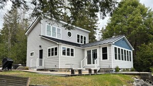 A two-story house with a covered patio area, a deck, and a stone retaining wall. - Maine Lake Cottage on Beech Hill Pond near Bar Harbor and Acadia National Park (Otis)