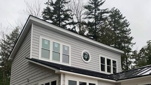 A two-story house with a deck, large windows, and a circular window on the second floor. - Maine Lake Cottage on Beech Hill Pond near Bar Harbor and Acadia National Park (Otis)