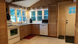 A compact kitchen with wooden cabinets, a stove, a dishwasher, and a microwave. - Maine Lake Cottage on Beech Hill Pond near Bar Harbor and Acadia National Park (Otis)