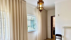 A hotel room with a bed, a chair, a window with curtains, a wooden floor, and a hanging light fixture. - Charming Villa in the CITY CENTER w/ OUTDOOR PATIO! FREEPARKING (Faro)