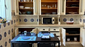 A kitchen with open cabinets, a dining table set for two, and a microwave on the counter. - Charming Villa in the CITY CENTER w/ OUTDOOR PATIO! FREEPARKING (Faro)