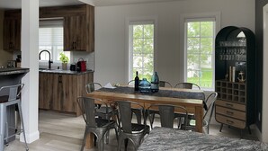 Una cocina moderna con armarios de madera, un comedor con una mesa de mármol y un mueble negro con cristalería.
