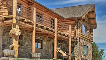 A log cabin with a stone exterior, a porch with a swing chair, and a large tree stump.