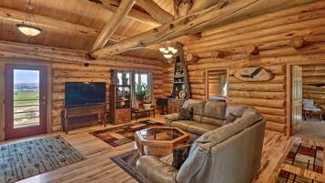 A log cabin interior with a large TV, leather sofa, wooden floors, and a fireplace.