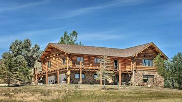 A large log cabin with a stone foundation, multiple windows, and a covered porch area.