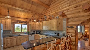 Eine Blockhausküche mit Holzausstattung, einer Granitarbeitsplatte und einer Barbereich mit rustikalen Barhocker.