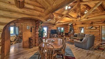 A log cabin interior with a wooden dining table, chairs, a sofa, and a television.