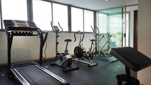 Un gimnasio con cintas de correr, bicicletas estáticas y una banca.
