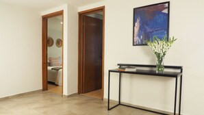 Un pasillo con una puerta de madera, una pequeña mesa con un jarrón de flores y un cuadro abstracto enmarcado en la pared.