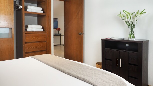 Una habitación de hotel con una cama, un armario de madera y un pequeño escritorio con un florero.