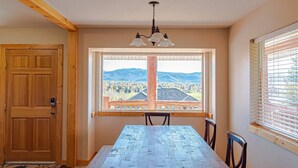 A dining area with a wooden table, chairs, a view of mountains, and a large window with blinds.