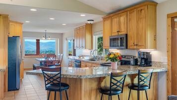A kitchen with wooden cabinets, a central island with bar stools, a refrigerator, and a view of mountains through a window.
