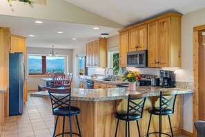 A kitchen with wooden cabinets, a central island with bar stools, a refrigerator, and a view of mountains through a window.
