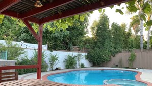 Ein Garten mit Schwimmbecken, Holzterrasse und einer Pergola.
