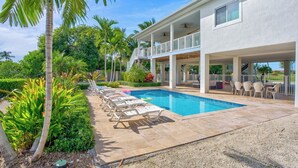 A poolside area with lounge chairs, a covered patio, and a view of a building with a balcony. - P98 - 75ft dock with shore power, 4 bed, 4 bath home w/private pool in Sombrero Beach Neighborhood. (Marathon)