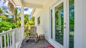 A covered balcony with a wooden railing, two chairs, a small stool, and a welcome mat. - P98 - 75ft dock with shore power, 4 bed, 4 bath home w/private pool in Sombrero Beach Neighborhood. (Marathon)